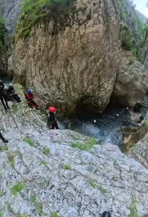 A canyoner in a wetsuit walking beneath huge sunlit boulders on the way into the canyon.
