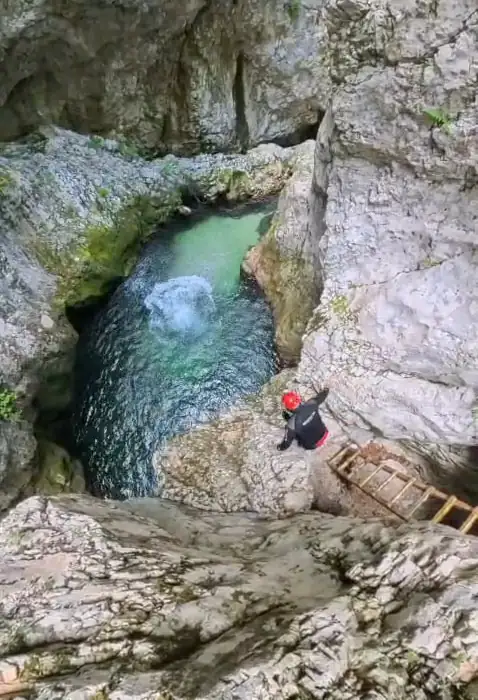 A canyoner descending rock into a clear turquoise pool below.